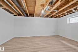 Unfinished ceiling with exposed joists and ductwork, white painted walls, wood-finish flooring, and a single window with blinds - 