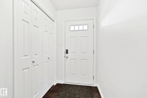 Entryway with wood-finish flooring, white paneled door with transom window, and built-in bi-fold closet - 9523 Simpson Crest Nw, Edmonton, AB 