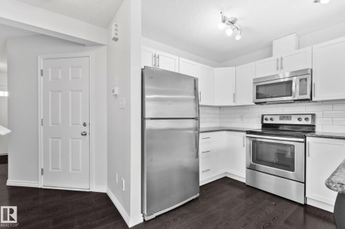 Kitchen featuring stainless steel appliances, white cabinetry, dark wood-finish flooring, and white subway tile backsplash - 9523 Simpson Crest Nw, Edmonton, AB 