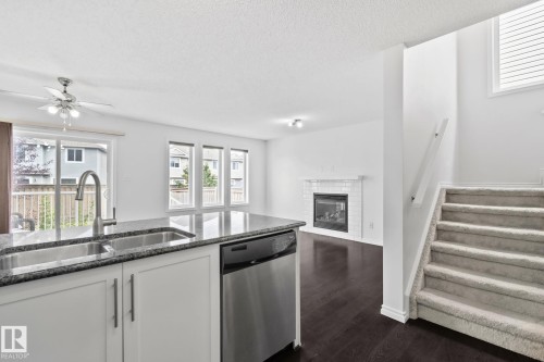 Kitchen island with integrated sink, stainless steel dishwasher, and stone-finish countertop - 9523 Simpson Crest Nw, Edmonton, AB 