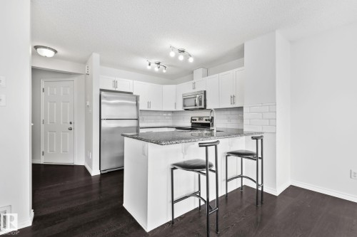 Kitchen featuring white cabinetry, stainless steel appliances, dark wood-finish flooring, and a stone countertop island with seating - 9523 Simpson Crest Nw, Edmonton, AB 