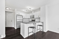 Kitchen featuring white cabinetry, stainless steel appliances, dark wood-finish flooring, and a stone countertop island with seating - 