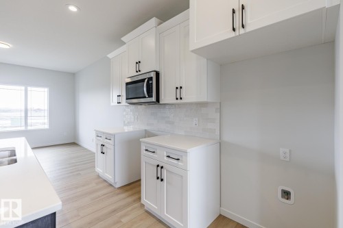 Contemporary kitchen featuring white cabinetry with black hardware, stainless steel microwave, light-toned wood-finish flooring, and a white subway tile backsplash - 3603 40 Avenue, Beaumont, AB - Indoor Photo Showing Kitchen With Double Sink