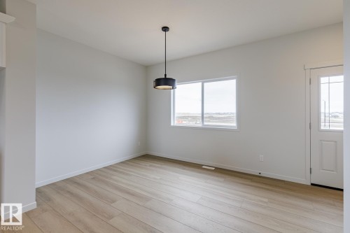 Open concept room featuring wood-finish flooring, a modern drum pendant light fixture, and a large window - 3603 40 Avenue, Beaumont, AB - Indoor Photo Showing Other Room