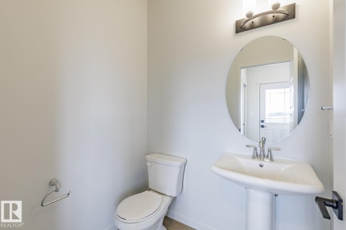 Pedestal sink with chrome fixtures and an oval mirror, complemented by an overhead vanity light - 3603 40 Avenue, Beaumont, AB - Indoor Photo Showing Bathroom