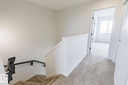 Carpeted hallway and staircase featuring light gray walls, white trim, and a white balustrade with a black handrail - 3603 40 Avenue, Beaumont, AB - Indoor Photo Showing Other Room