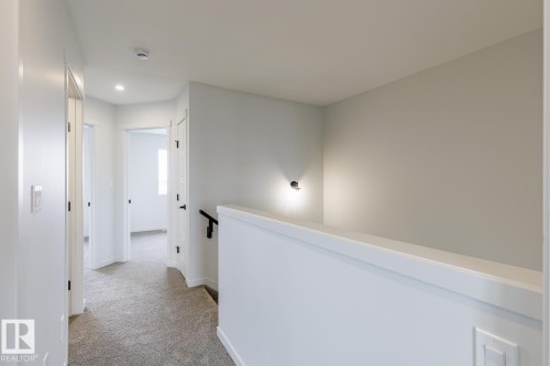 Carpeted hallway with white walls and trim, featuring recessed lighting and a sleek black handrail - 3603 40 Avenue, Beaumont, AB - Indoor Photo Showing Other Room