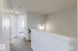 Carpeted hallway with white walls and trim, featuring recessed lighting and a sleek black handrail - 
