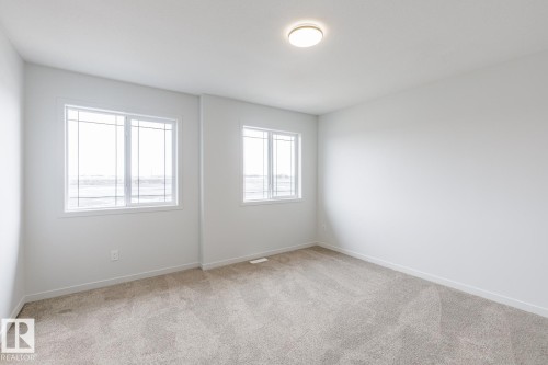 Bright interior room featuring two windows with white frames and grids, light neutral carpeting, white baseboards, and a flush-mount ceiling light fixture - 3603 40 Avenue, Beaumont, AB - Indoor Photo Showing Other Room