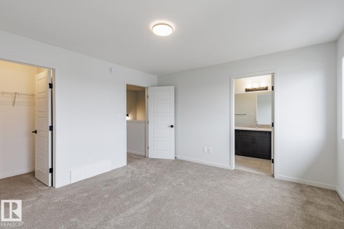Carpeted bedroom featuring a flush-mount ceiling light, white walls, and a walk-in closet with wire shelving - 3603 40 Avenue, Beaumont, AB - Indoor