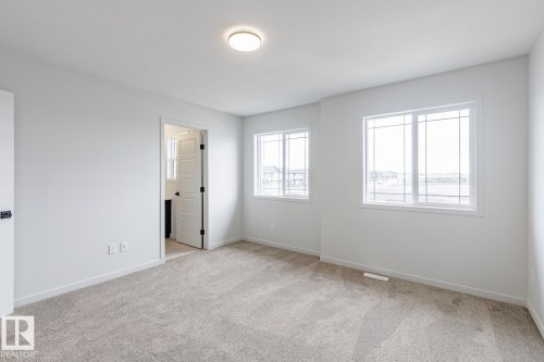 Spacious room featuring neutral carpeting, white walls, two multi-pane windows, a flush-mount ceiling light, and a white interior door with black hardware - 3603 40 Avenue, Beaumont, AB - Indoor Photo Showing Other Room