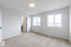 Spacious room featuring neutral carpeting, white walls, two multi-pane windows, a flush-mount ceiling light, and a white interior door with black hardware - 