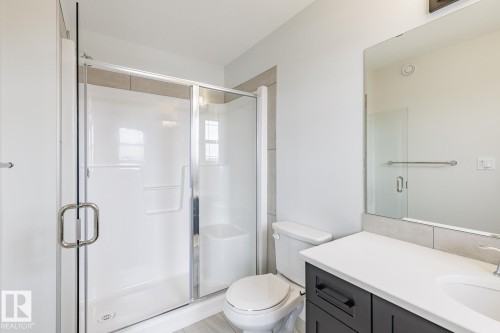 Bathroom featuring a white shower stall with glass enclosure and chrome hardware, a dark wood-finish vanity with a white countertop and integrated sink, a large wall-mounted mirror, and light-toned wall tile accents - 3603 40 Avenue, Beaumont, AB - Indoor Photo Showing Bathroom