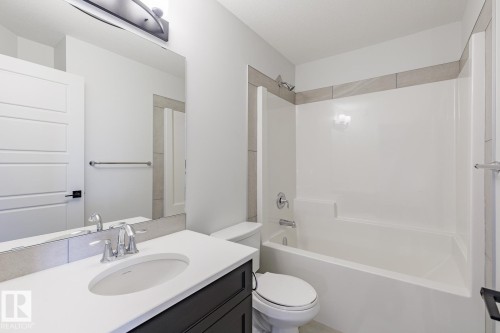 Bathroom featuring a white bathtub/shower combination, dark wood-finish vanity with white countertop, chrome fixtures, and a large wall mirror - 3603 40 Avenue, Beaumont, AB - Indoor Photo Showing Bathroom