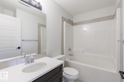 Bathroom featuring a white bathtub/shower combination, dark wood-finish vanity with white countertop, chrome fixtures, and a large wall mirror - 