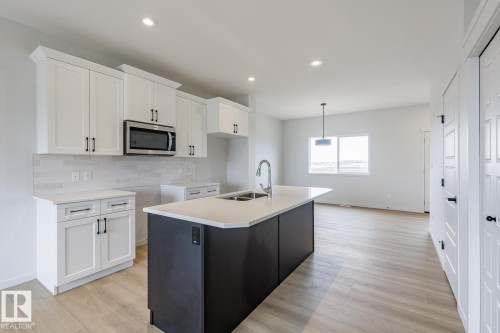 Modern kitchen featuring a dark-toned island with an undermount double-basin sink and an arched faucet - 3603 40 Avenue, Beaumont, AB - Indoor Photo Showing Kitchen With Double Sink