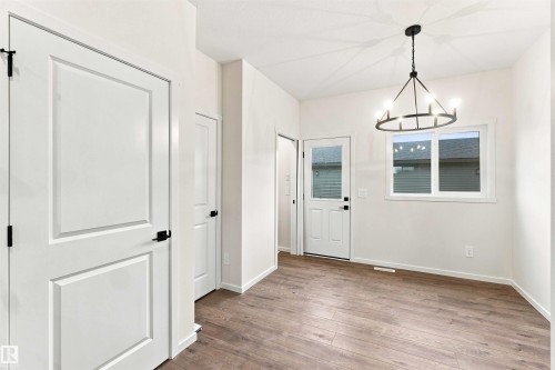Wood-finish flooring, white paneled doors with black hardware, and a modern circular chandelier with exposed bulbs - 7097 Rosenthal Drive Nw, Edmonton, AB 