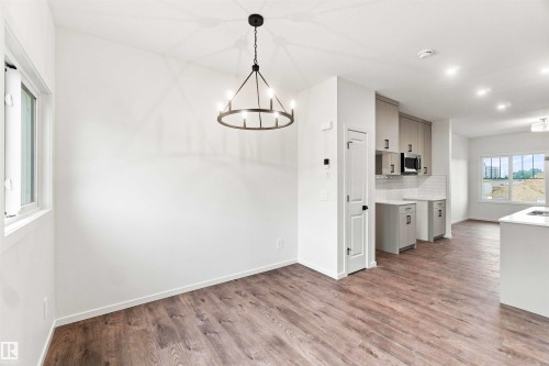 Open-concept living area featuring wood-finish flooring, a modern chandelier, recessed lighting, white walls, and a kitchen with light-toned cabinetry and a subway tile backsplash - 7097 Rosenthal Drive Nw, Edmonton, AB 
