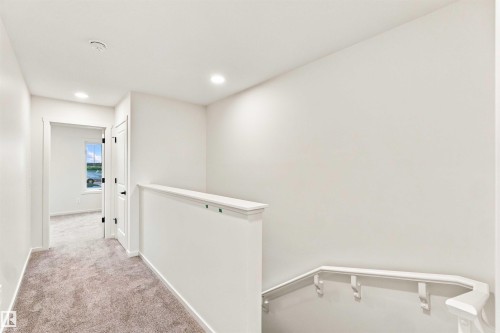 Carpeted hallway with white walls and ceiling, featuring recessed lighting and a white staircase handrail - 7097 Rosenthal Drive Nw, Edmonton, AB 