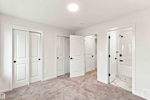 Plush carpet flooring, multiple panel doors with matte black hardware, recessed ceiling lighting, and a bathroom featuring a subway-tiled shower and patterned floor tile - 7097 Rosenthal Drive Nw, Edmonton, AB 