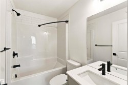 White subway tile tub surround, matte black shower fixtures, vanity with integrated sink, matte black vanity faucet, and a large wall-mounted mirror - 