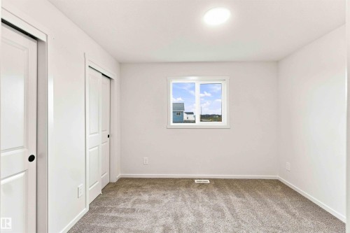 Neutral tone wall paint, light-colored carpet flooring, white trim, sliding closet doors, and a ceiling-mounted light fixture - 7097 Rosenthal Drive Nw, Edmonton, AB 