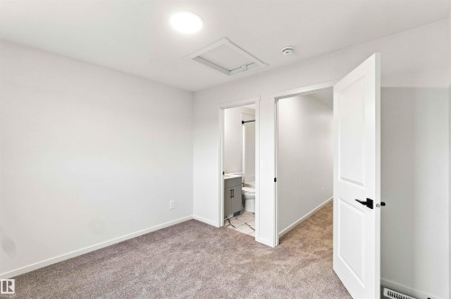 Carpeted interior space with white walls, a flush-mounted ceiling light, and white panel doors with black hardware - 7097 Rosenthal Drive Nw, Edmonton, AB 