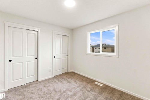 Plush carpeting, light neutral wall paint, white trim, sliding closet doors with black hardware, and a window with white framing - 7097 Rosenthal Drive Nw, Edmonton, AB 