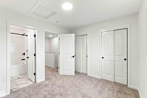 Plush carpeted flooring, white interior doors with matte black hardware, and two panel sliding closet doors - 7097 Rosenthal Drive Nw, Edmonton, AB 