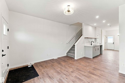 Wood-finish flooring, staircase with carpeted treads and white handrail, recessed lighting, white perimeter walls, and a built-in wet bar with white subway tile backsplash - 7097 Rosenthal Drive Nw, Edmonton, AB 