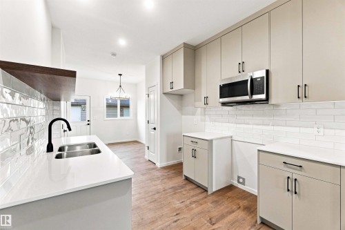 Light-toned cabinetry with matte black hardware, white countertops, stainless steel over-range microwave, subway tile backsplash, and wood-finish flooring - 7097 Rosenthal Drive Nw, Edmonton, AB 