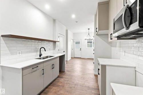 Kitchen featuring wood-finish flooring, light-toned cabinetry with dark hardware, a subway tile backsplash, white countertops, and a stainless steel microwave - 7097 Rosenthal Drive Nw, Edmonton, AB 