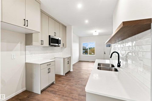 Contemporary kitchen featuring light cabinetry, stainless steel microwave, white subway tile backsplash, and wood-finish flooring - 7097 Rosenthal Drive Nw, Edmonton, AB 