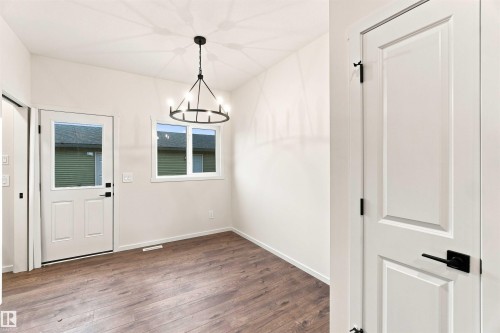 Wood-finish flooring, white walls, black chandelier, white paneled doors with black hardware, and white trim throughout - 7097 Rosenthal Drive Nw, Edmonton, AB 
