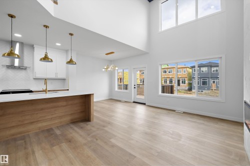 Open-concept living space featuring wood-finish flooring, a kitchen island with a light wood finish, white cabinetry, high ceilings, and expansive windows - 1780 Crossbill Loop Nw, Edmonton, AB 