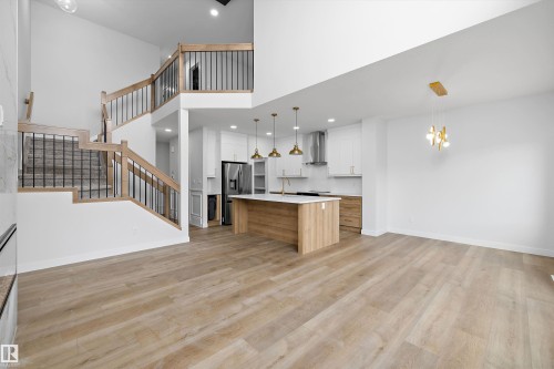 Bright open-concept living area with light wood-finish flooring, a contemporary kitchen island with a light-colored countertop, and a double-height ceiling - 1780 Crossbill Loop Nw, Edmonton, AB 