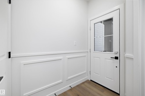 White panel door with clear glass insert, wainscoting detailing, wood-finish flooring, and black hardware - 1780 Crossbill Loop Nw, Edmonton, AB 