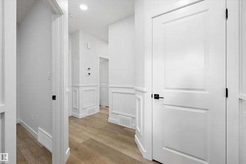 White paneled doors with matte black hardware, wood-finish flooring, and crisp white wainscoting - 1780 Crossbill Loop Nw, Edmonton, AB 