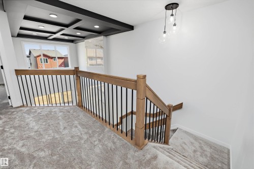 Staircase featuring wood railings with black balusters, a contemporary chandelier, and a coffered ceiling with recessed lighting - 1780 Crossbill Loop Nw, Edmonton, AB 