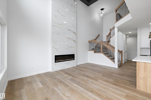Two-story living area featuring a full-height fireplace with a linear insert, wood-finish flooring, a contemporary staircase with iron balusters and wood handrails, and a recessed ceiling - 1780 Crossbill Loop Nw, Edmonton, AB 