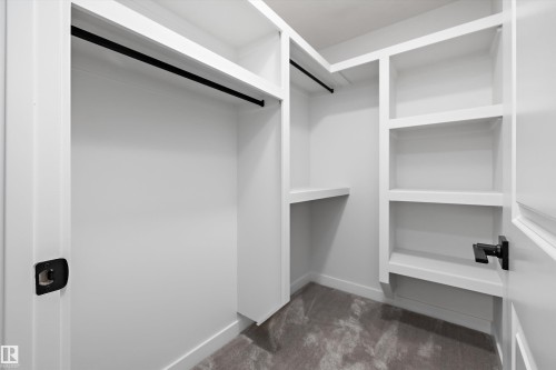 Walk-in closet featuring white built-in shelving, black hanging rods, and gray carpeting - 1780 Crossbill Loop Nw, Edmonton, AB 