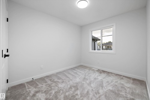Neutral wall color, grey patterned carpet, white window trim, white door with black hardware, and an overhead light fixture - 1780 Crossbill Loop Nw, Edmonton, AB 