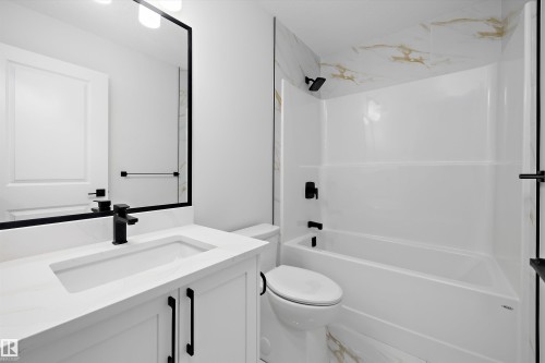 White vanity with integrated sink, black fixtures, framed mirror, and a white bathtub with a tiled surround - 1780 Crossbill Loop Nw, Edmonton, AB 
