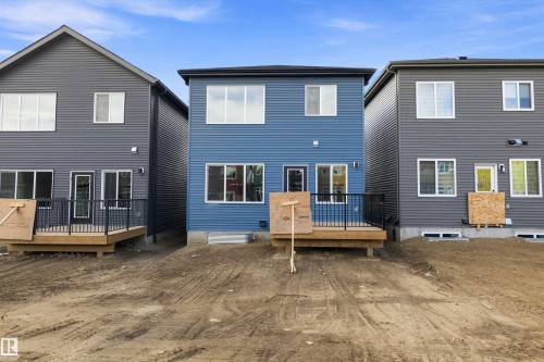 Rear exterior showcasing blue horizontal siding, multiple large windows, and a wood-finish deck with black railings - 1780 Crossbill Loop Nw, Edmonton, AB 