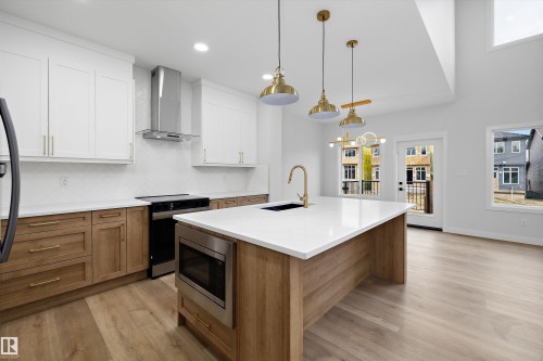Kitchen with dual-toned cabinetry, a large center island with a white countertop, and wood-finish flooring - 1780 Crossbill Loop Nw, Edmonton, AB 