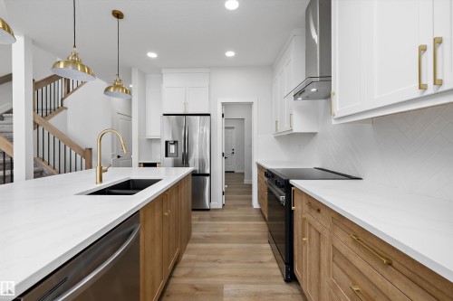 Kitchen featuring white upper cabinetry, wood-finish lower cabinetry, and stainless steel appliances - 1780 Crossbill Loop Nw, Edmonton, AB 