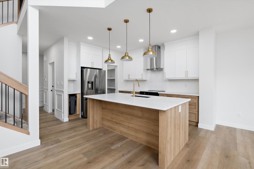 Open-concept kitchen with a large island, white shaker cabinetry, stainless steel appliances, and wood-finish flooring - 1780 Crossbill Loop Nw, Edmonton, AB 