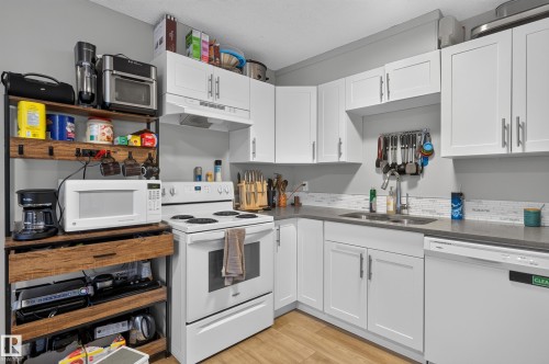 White cabinetry with brushed nickel hardware, solid surface countertops, white subway tile backsplash, and wood-finish flooring - 18319 93 Avenue Nw, Edmonton, AB 