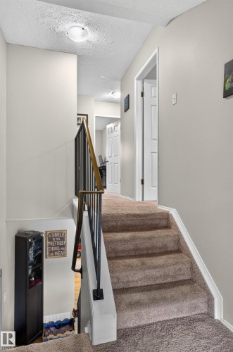 Carpeted staircase featuring a metal and wood-finish railing, leading to a hallway with a flush-mount ceiling light - 18319 93 Avenue Nw, Edmonton, AB 