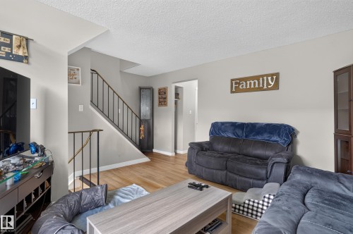 Wood-finish flooring, staircase with dark metal railings, light gray wall paint, and white trim - 18319 93 Avenue Nw, Edmonton, AB 